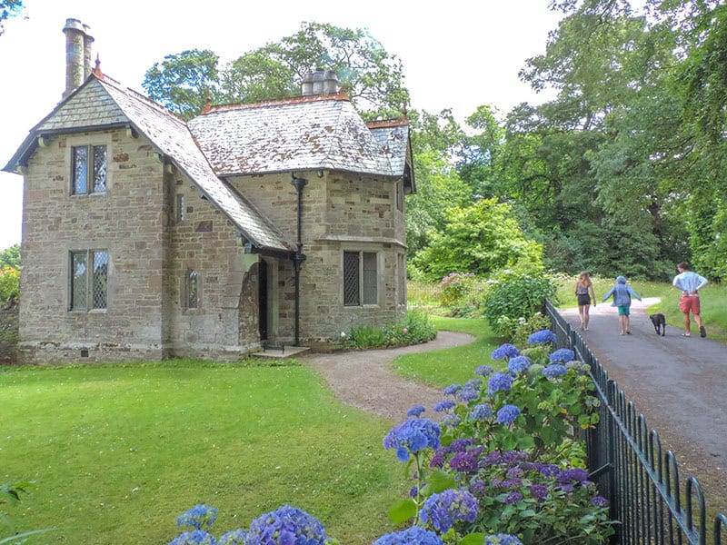 people with a dig walking by an iold house near Falmouth  - one of the places to visit in cornwall