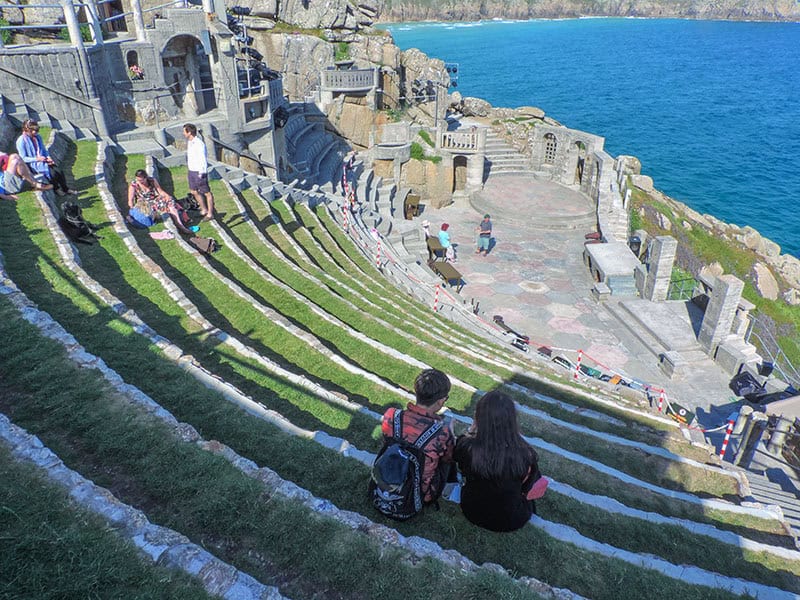 a couple sitting on steps in a Greek theater overlooking the sea.