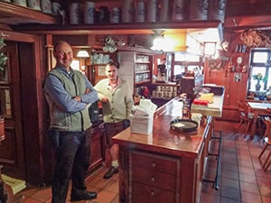 two men standing behind a bar visited on a day trip from Munich