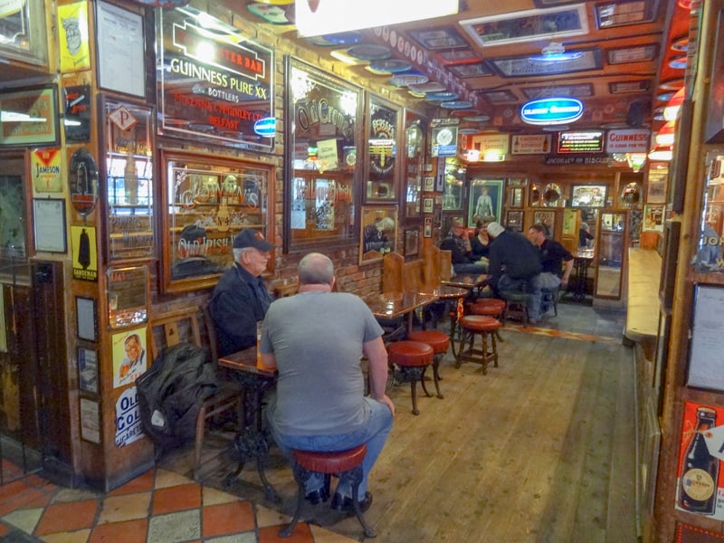 Men sitting a tables in an ornate bar with many mirrors and posters on the wall
