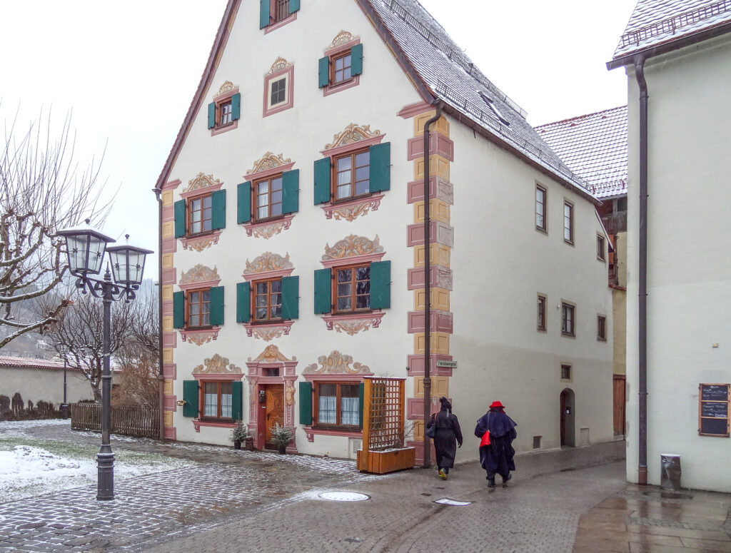 people walking by a an ornate house with green shutters in one of the places to visit in Bavaria