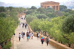 people walking along a wide parh near a temple while seeing Sicily by car