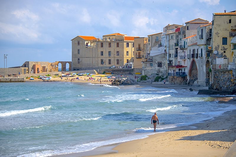 a man walking along the seashore in an old city