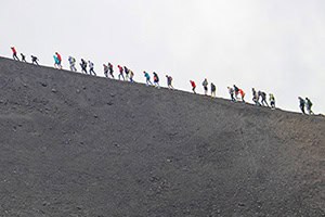 a line of hikers walking up the slope of a volcano