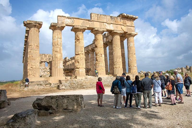 a group standing in front of an ancient temple while seeing Sicily by car