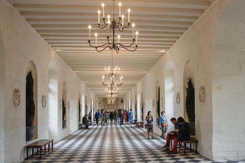 people walking through a long Gallery with chandeliers above