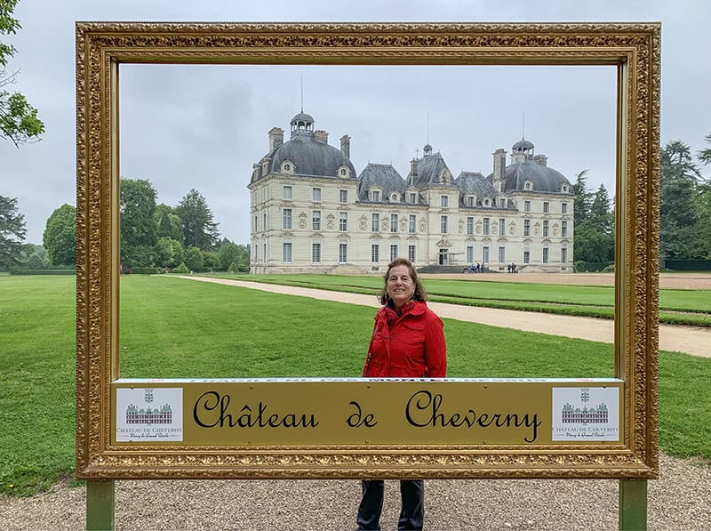 a woman looking through a large picture frame in front of a chateau