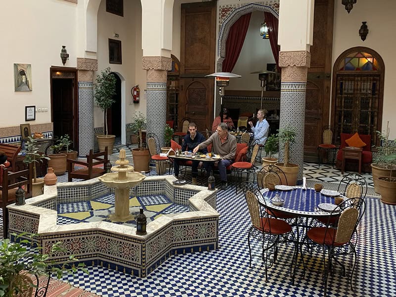 people sitting near a large tiled fountain in an Arabesque hotel lobby