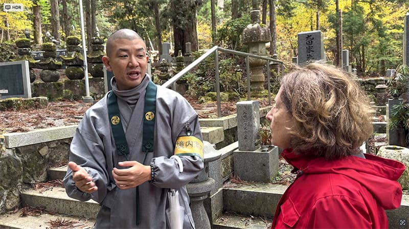 a monk speaking with a woman in a red jacket in koyasan japan