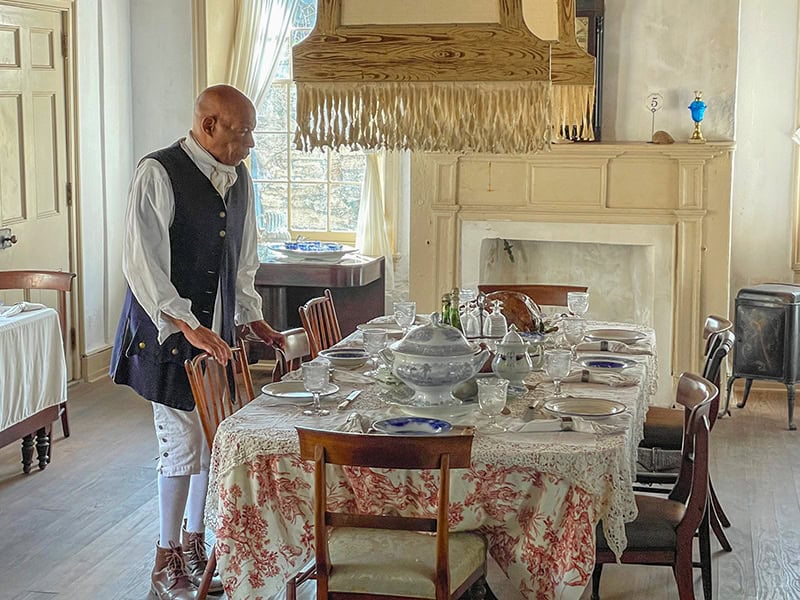 A black actor standing by a table covered with old china seen on a trip from Orlando to Amelia Island