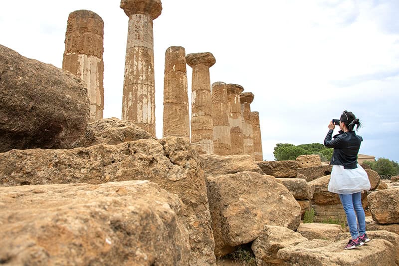 a young woman taking a photo of an ancient temple in Agrigento Sicily